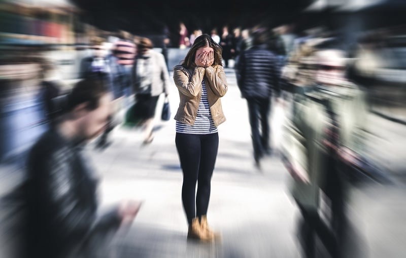 young woman covering face with hands in a crowd of people