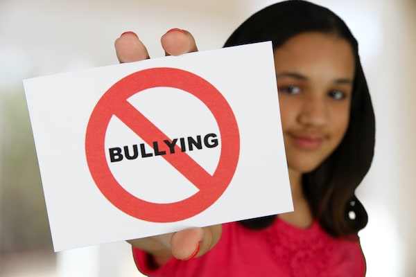 Child Holding Card Depicting No Bullying Held Out To Camera